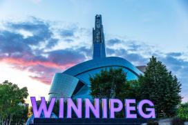 Das architektonisch eindrucksvolle Gebäude des Canadian Museum for Human Rights. Im Vordergrund in großen Leuchtbuchstaben der Schriftzug "Winnipeg"
