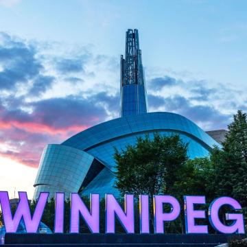 Das architektonisch eindrucksvolle Gebäude des Canadian Museum for Human Rights. Im Vordergrund in großen Leuchtbuchstaben der Schriftzug "Winnipeg"