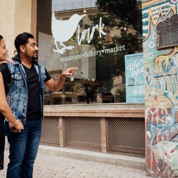 Ein Paar steht in den Straßen des Exchange Districts und betrachtet eine bunte Graffiti Wand, auf der eine Hinweistafel zur Geschichte des Viertels installiert wurde.