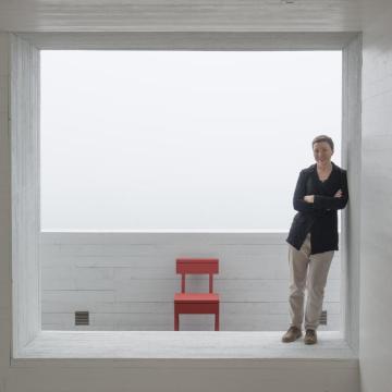 Zita Cobb, Social Entrepreneur, lehnt an einer Wand in einem weißen Raum, im Hintergrund ein roter Stuhl, 