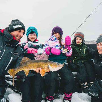Eine Familie hält an einem Wintertag einen frisch gefangenen Fisch vor die Kamera.