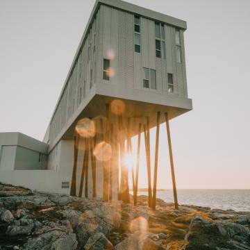 DAs Fogo Island Inn steht auf Felsen, im Hintergrund ist der Sonnenuntergang zu sehen.