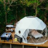 Das Kuppelzelt von Moonlit Canopy steht auf einer Holzterrasse mit schönem Möbel und Whirlpool.