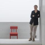 Zita Cobb, Social Entrepreneur, lehnt an einer Wand in einem weißen Raum, im Hintergrund ein roter Stuhl, 