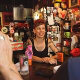 Eine Barfrau steht hinter einem Tresen einer Bar und lächelt