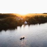 Ein Kanu paddelt bei den Flying Dust First Nations, im Hintergrund steht am Flussufer ein Tipi