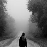Eine Frau geht im Nebel eine einsame Schotterstraße entlang.