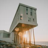 DAs Fogo Island Inn steht auf Felsen, im Hintergrund ist der Sonnenuntergang zu sehen.